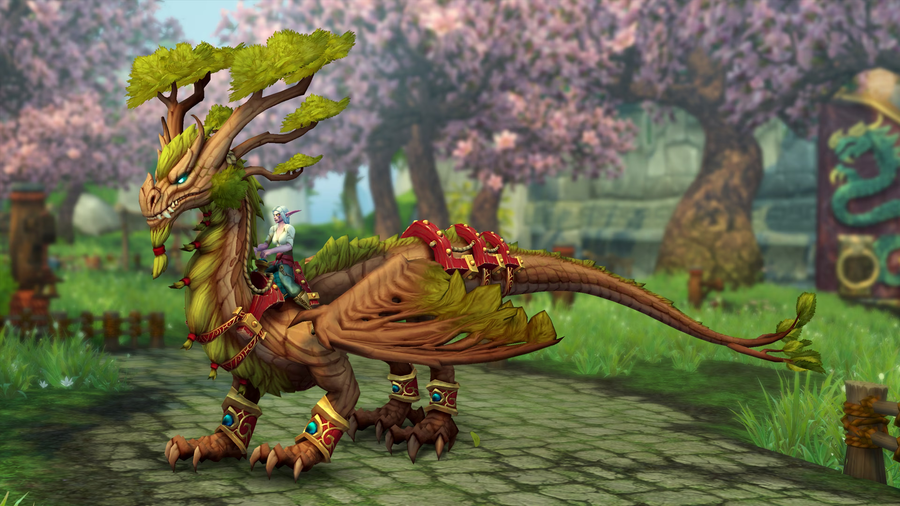 A sleek dragon mount standing on the ground. Its skin looks like wood and it has green, leafy branches for antlers or horns. It is ridden by a female night elf in green travelling garb. The blurred background appears to be cherry blossom trees in Pandaria.